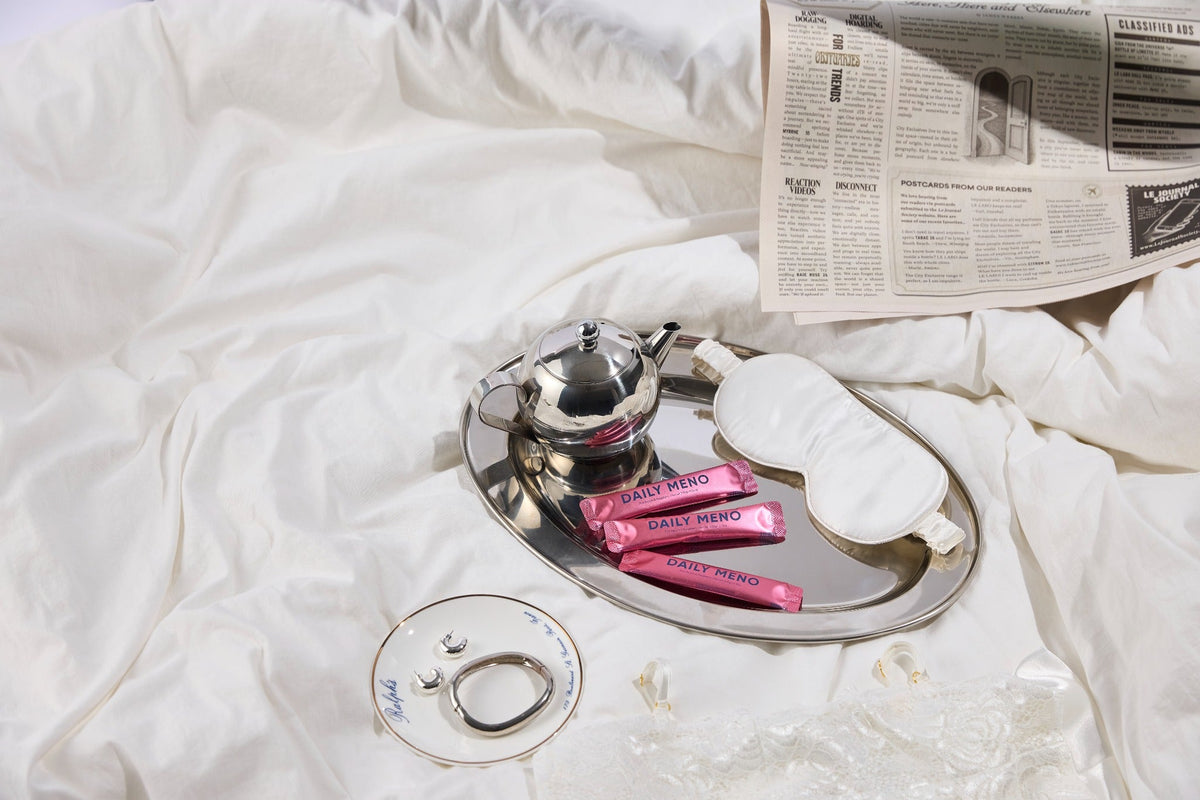 Daily Meno sachets styled with a tea service and sleep mask for a menopause wellness routine